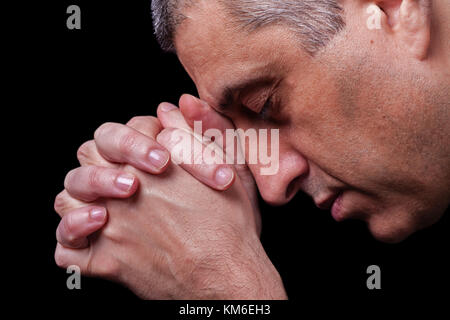 Close up of faithful mature man praying hands folded worship god head down and eyes closed in religious black background religion portrait Christian Stock Photo