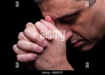 Close up of faithful mature man praying hands folded worship god head down and eyes closed in religious black background religion portrait Christian Stock Photo