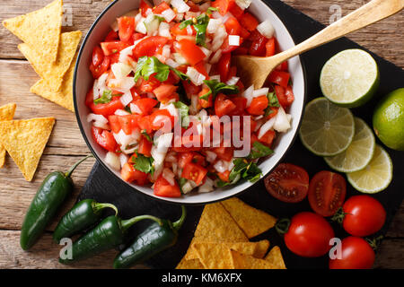 Mexican pico de gallo from tomatoes, onions, cilantro and jalapeno pepper close-up in a bowl and nachos on a table. horizontal top view from above Stock Photo