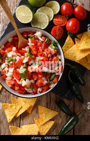Mexican pico de gallo from tomatoes, onions, cilantro and jalapeno pepper close-up in a bowl and nachos on a table. Vertical top view from above Stock Photo