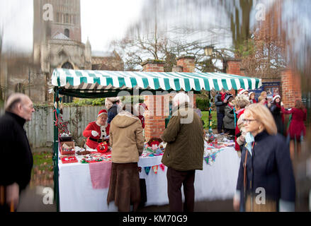 Stall holders dressed as Santa at the Farmers and Craft market outside Tewkesbury Abbey with Christmas carol singers Stock Photo