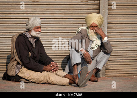 Two Punjabi Sikh men with white beards and turbans sit talking in the street, at Amritsar, Punjab Stock Photo