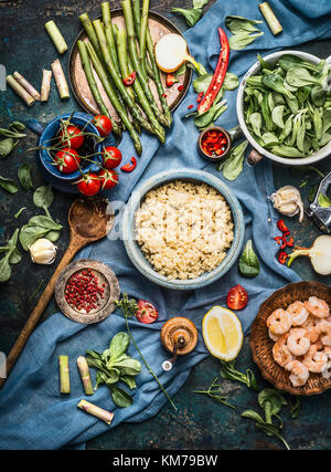 Cooked quinoa with green asparagus and other vegetables ingredients for healthy cooking on dark rustic kitchen table background with cooking spoon and Stock Photo