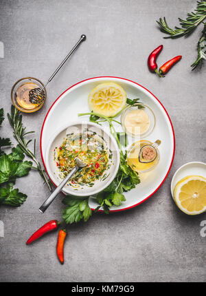 Homemade sauce or salad dressing in bowl with ingredients:  fresh herbs, oil, lemon and honey on gray concrete background, top view, flat lay. Healthy Stock Photo