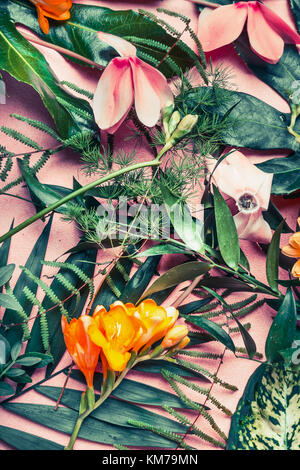 Various green tropical leaves and exotic flowers , nature flat lay on pastel pink background, top view Stock Photo