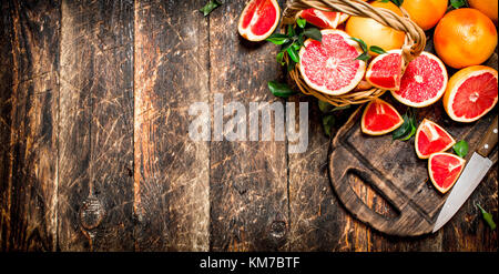 Sliced pieces of grapefruit with a knife. On wooden background. Stock Photo