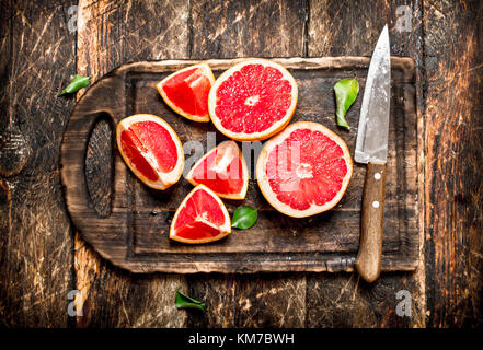 Sliced pieces of grapefruit with a knife. On wooden background. Stock Photo