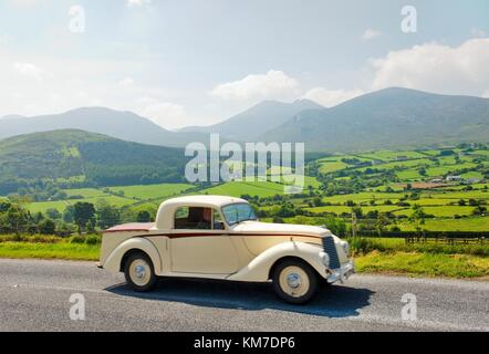 Vintage car tourer on the Trassey Road through the Mourne Mountains, County Down, Ireland with Slieve Bearnagh in the distance. Stock Photo