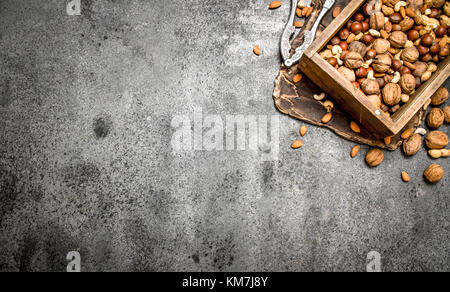 Various nuts in an old box and nutcracker. On rustic background. Stock Photo
