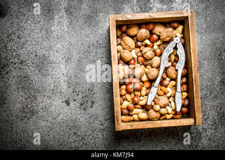 Various nuts in an old box and nutcracker. On rustic background. Stock Photo