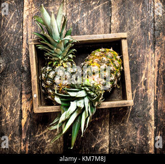 Fresh pineapple in an old box. On wooden background. Stock Photo