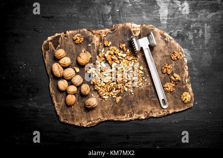Crushed walnuts with a hammer on the old Board. On a black chalkboard Stock Photo