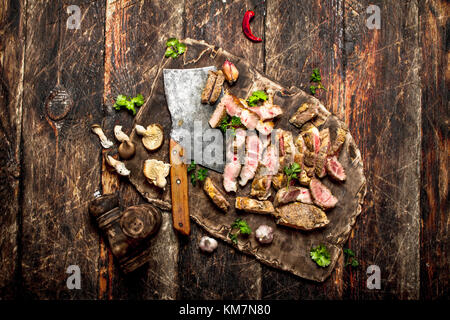 Meat grill. Sliced grilled pork with an old hatchet ,spices and herbs .On the old wooden table. Stock Photo