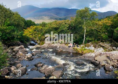 Young man and woman picnic beside Galway’s River at Galway’s Bridge above Upper Lake, Killarney National Park, Co.Kerry, Ireland Stock Photo