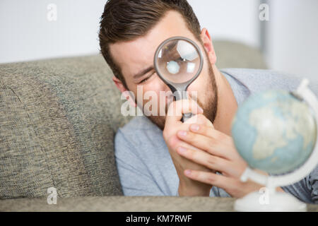 man considering a world globe with a magnifying glass Stock Photo