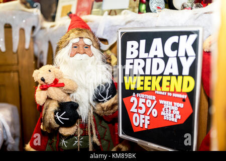 Santa Claus or Father Christmas dummy figure or mannequin on display holidng a teddy bear in a toy shop window next to a 25% off Black Friday sign in  Stock Photo