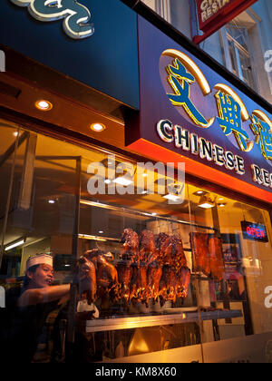 CRISPY DUCK CHINATOWN CHINA TOWN SOHO LONDON Chef arranging rows of enticing Peking crispy duck and pork belly ribs hanging air drying in Chinese restaurant at dusk, Gerrard Street Chinatown Soho London Stock Photo