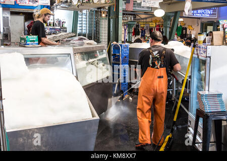 Seattle, Washington, USA - September 4th, 2017: Male worker wearing a waterproof fishing pants is cleaning the floor at Pike Place Fish with a pressur Stock Photo