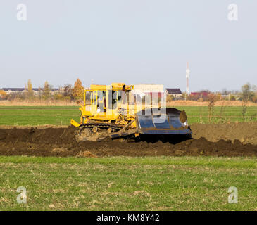 The yellow tractor with attached grederom makes ground leveling. Work on the drainage system in the field. Stock Photo