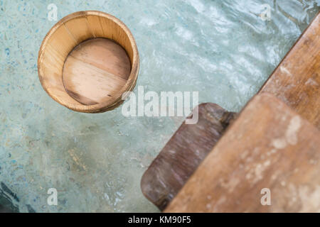 japanese style hot springs with wooden barrel scoop floating on water and water flowing. Stock Photo