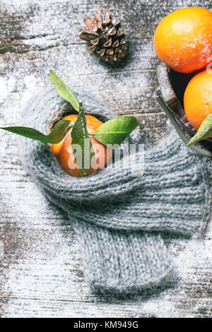 Tangerine in scarf over wooden background with snow and cone. Top view. Stock Photo