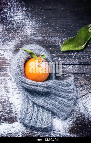 Tangerine in scarf over wooden background with snow and leaf. Top view. Stock Photo