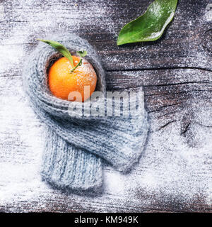 Tangerine in scarf over wooden background with snow and leaf. Top view. Square image Stock Photo