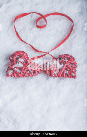 Two beautiful romantic vintage red hearts tied together with a ribbon on a white snow winter background. Love and St. Valentines Day concept. Stock Photo
