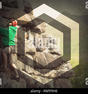 Focused man climbing a large rock face with mountains in the background Stock Photo