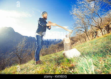 Young man with lumberjack beard cuts wood. Stock Photo