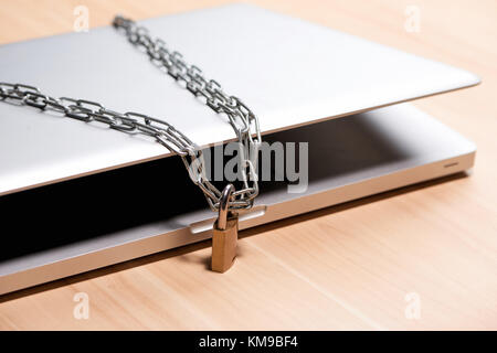 Heavy chain with a padlock around a laptop on table. Stock Photo