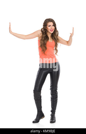 Grimacing woman standing with arms outstretched and pressing fake walls. Full length studio shot isolated on white. Stock Photo
