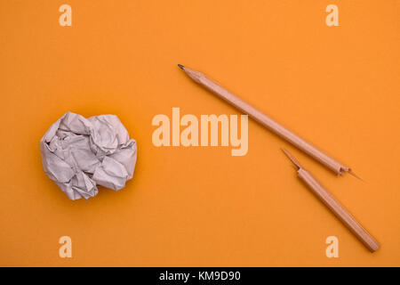 Broken pencil and crumpled paper ball on a yellow background. Close up. Stock Photo