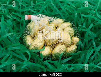 A mesh bag of gold foil wrapped chocolate Easter candy eggs in shredded plastic green grass. Stock Photo