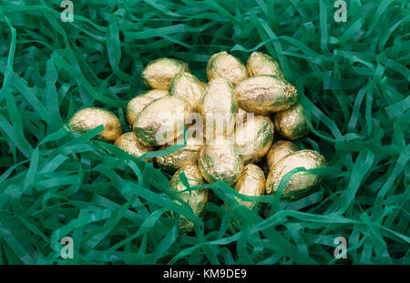 A pile of gold foil wrapped chocolate Easter candy eggs nestled in shredded plastic green grass. Stock Photo