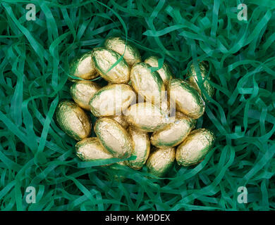 Top view of a pile of gold foil wrapped chocolate Easter candy eggs nestled in shredded plastic green grass. Stock Photo