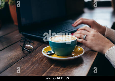 Cup of coffee next to a woman using laptop Stock Photo