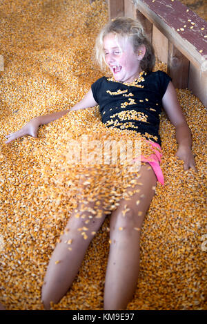 Girl messing about in a vat of corn on a farm Stock Photo