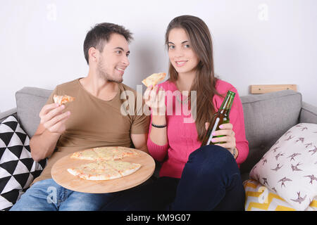 Beautiful young couple drinking beer and eating pizza. Indoors. Stock Photo