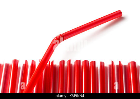 Row of red plastic straws with one straw sticking out over white background Stock Photo