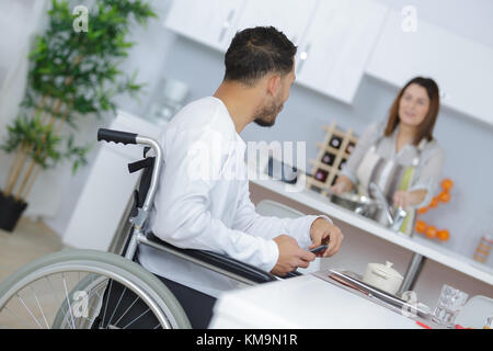 Man in wheelchair talking to partner who is preparing meal Stock Photo