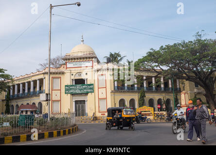 Exterior of Government Ayurveda Medical College and Hospital, people walking and driving vehicles on road in foreground at Mysore, Mysuru, Karnataka,  Stock Photo