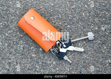 A bunch of keys in a leather case lying on the ground. Keys in the leather partholme were lost or found Stock Photo