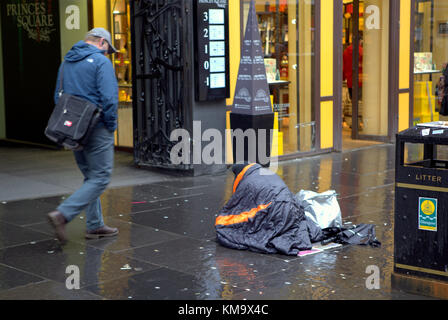 homeless man in a sleeping bag on buchanan  street on the style mile with possessions begging in front of the upmarket princes square shopping centre