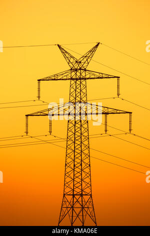 High-voltage electricity pylon / transmission tower silhouetted against sunset Stock Photo