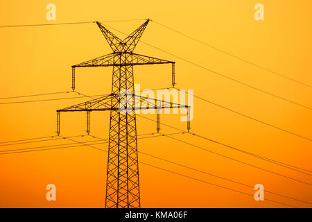 High-voltage electricity pylon / transmission tower silhouetted against sunset Stock Photo