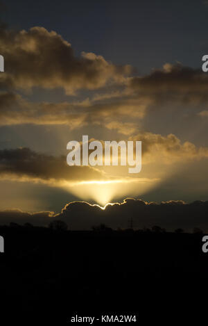 lightrays from the sun rising behind some clouds Stock Photo