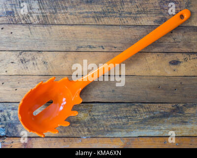 orange plastic spaghetti draining utensil on wood table Stock Photo