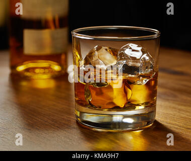 https://l450v.alamy.com/450v/kma9h7/glass-of-whiskey-on-ice-with-bottle-on-wood-bar-kma9h7.jpg