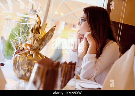 Young brunette sitting in a restaurant and looking out the window Stock Photo